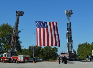 an image of first responders raising the American Flag during the MBA's 9/11 Memorial Vehicle Show